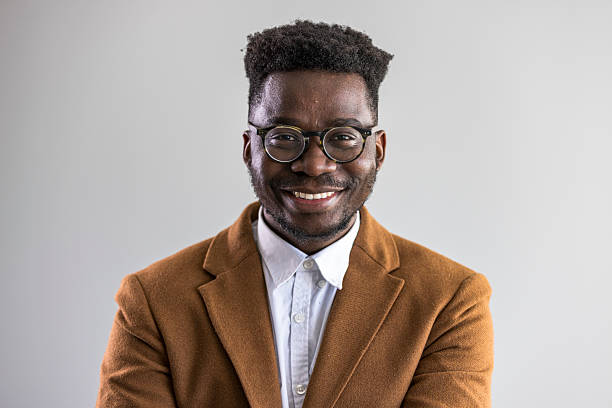A confident Nigerian man in glasses and a brown blazer, smiling